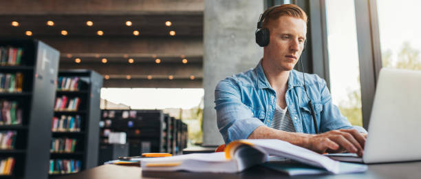 istock Male student working on laptop at public library 1284545597