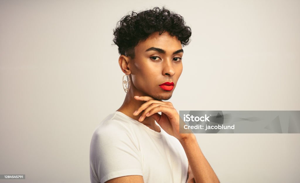 Handsome gay man with make up Portrait of a handsome gay man with make up. Transgender male with red lip stick and earring looking at camera. Transgender Person Stock Photo