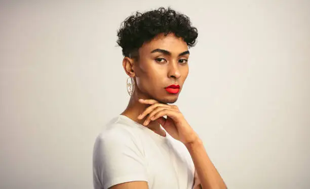 Portrait of a handsome gay man with make up. Transgender male with red lip stick and earring looking at camera.