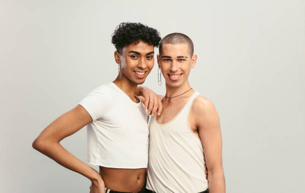 Happy gay community members Portrait of a two handsome gay men standing together. Two male friends with earrings looking at camera on white background. gender fluid photos stock pictures, royalty-free photos & images