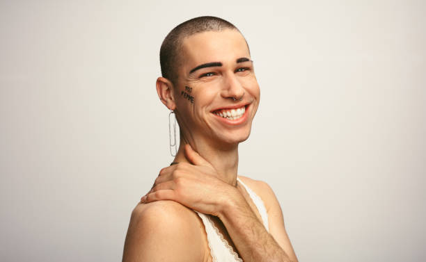 Gender fluid man smiling on white background Portrait of a young gay man wearing earring looking happy on white background. Gender fluid man smiling on white background. queer man facing camera stock pictures, royalty-free photos & images