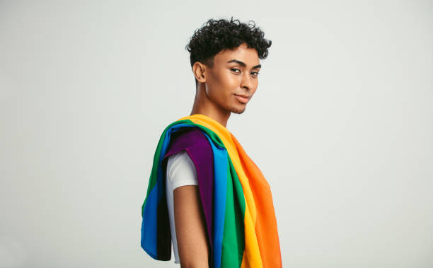 Man with a gay pride flag Handsome young man with pride movement LGBT Rainbow flag on shoulder against white background. Man with a gay pride flag looking at camera. gender fluid photos stock pictures, royalty-free photos & images