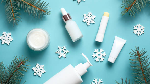 istock Set of winter skincare cosmetics on blue background. Packaging design template. Moisturizer cream jar, lipstick, pump bottle, tube, snowflakes and fir tree branches. Flat lay, top view. 1284548394
