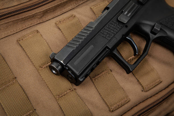 istock A modern black pistol on a brown military backpack. Weapons for defense and attack. Arming the police, army and special units. 1284550794