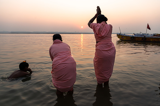 woman  with reflection on the water of river ganges doing rituals with beautiful sunrise at varanasi.Smokey atmospher