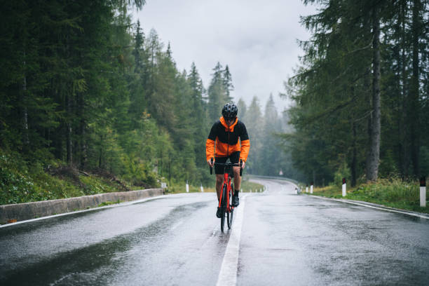 road bicyclist rides up a wet road in the rain - rain drenched men wet imagens e fotografias de stock