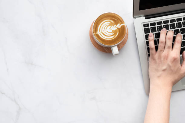 istock Man hand is typing on laptop computer keyboard over white marble office desk table with a cup of latte coffee. Top view with copy space, flat lay. 1284555609