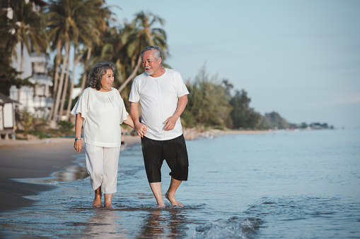 The romantic Asian senior couple hand in hand while walking on summer beach sunset. Travel leisure and activity after retirement on vacations and summer concept. Vacation and relaxation time.