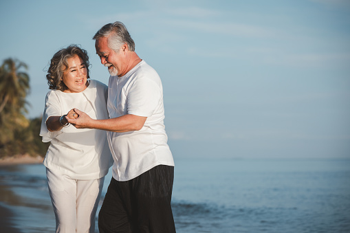 The romantic Asian senior couple dancing while standing on summer beach sunset. Travel leisure and activity after retirement on vacations and summer concept. Vacation and relaxation time.