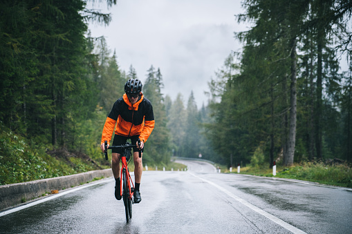Road bicyclist rides up a wet road in the rain