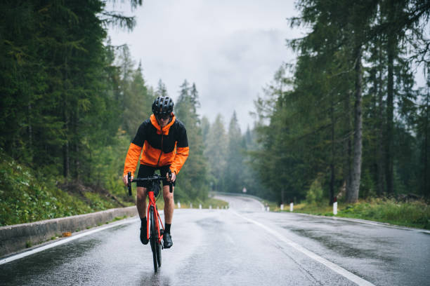 Road bicyclist rides up a wet road in the rain stock photo