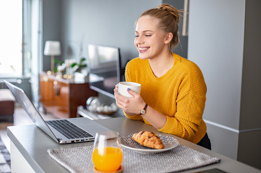 Young woman drinking morning coffee and using laptop