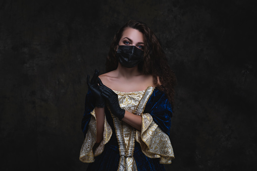 Hermosa mujer en vestido renacentista, máscara facial y guantes sobre fondo oscuro abstracto photo