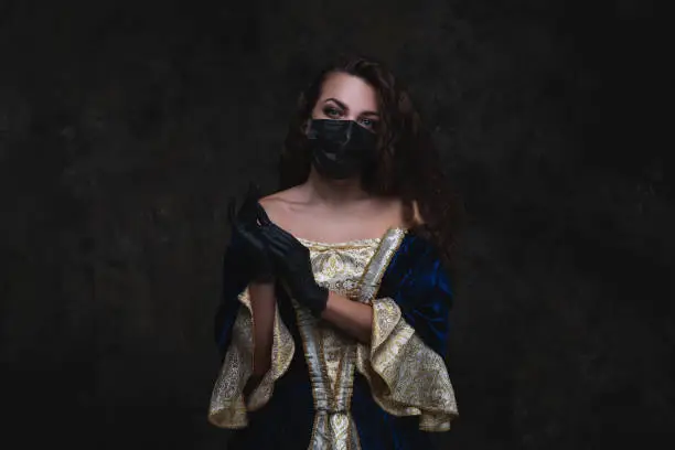 Beautiful woman in renaissance dress, face mask and gloves on abstract dark background, old and new concept