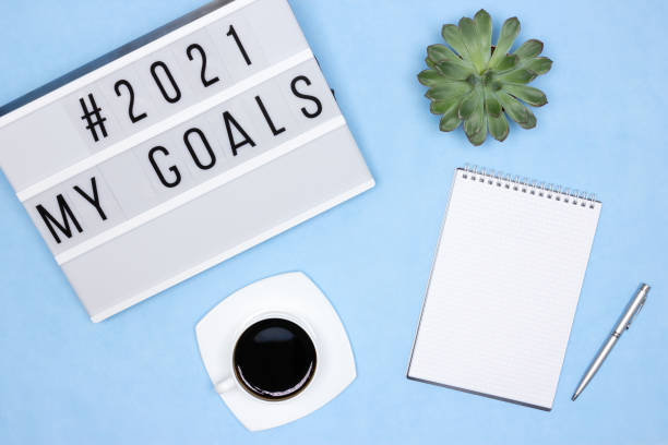 istock Office workplace - top view. Notebook, pen, coffee cup, succulent, lightbox with 2021 My Goals text on blue desk. Plans for the coming year concept 1284571832