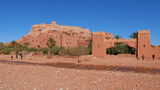 Tourists shooting pictures with a camel below historic Moorish ksar Ait Benhaddou, UNESCO World Heritage Site, with historic loam buildings located near  Ouarzazate, Morocco, Africa.