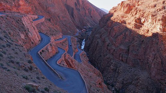 Aerial view of curvy serpentine road at a narrow passage of famous Dadès Gorges in the southern Atlas Mountains near Boumalne Dadès, Morocco, Africa in the shadow of the bright morning light.