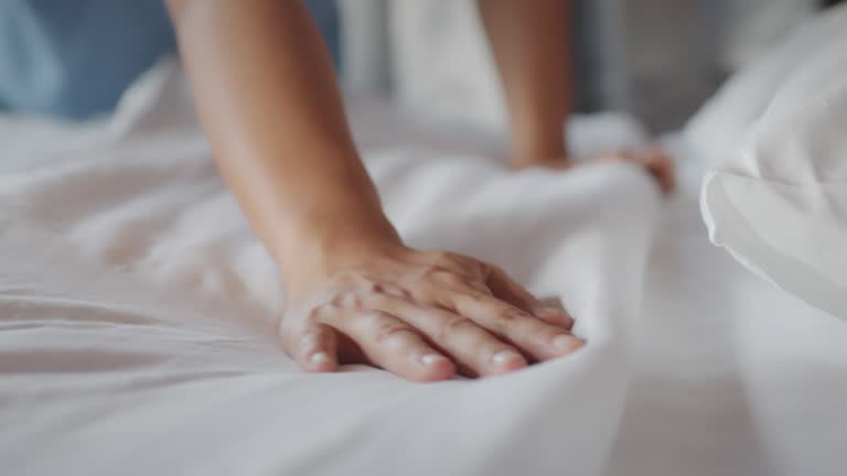 Asian woman cleaning bed arranging blanket and bedding in her bedroom after wake up in the morning time.