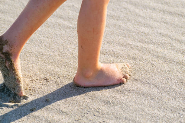 Boy dragging toe through the sand on a sunny afternoon stock photo