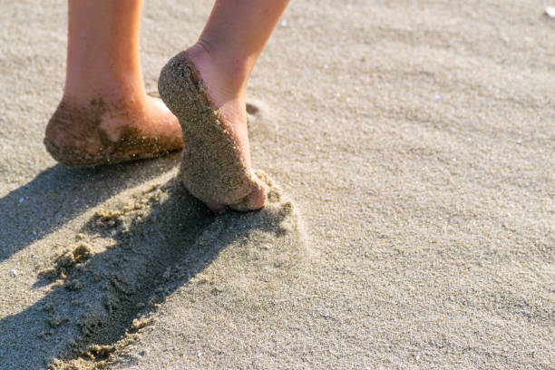 Boy dragging toe through the sand on a sunny afternoon stock photo