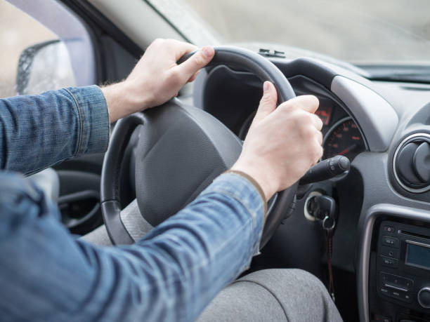 istock Human arms in denim sleeves on steering wheel, inside cab view, close up, selective focus. Ordinary man driving a car. 1284576999