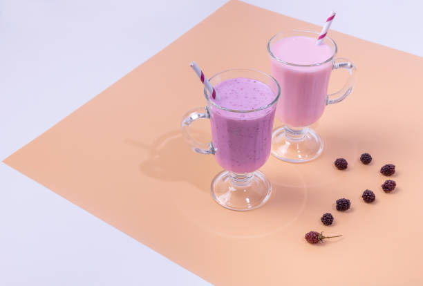 deux verres de smoothies blackberry et framboise sur un fond coloré. le concept d’une alimentation saine - milk shake smoothie blackberry isolated photos et images de collection