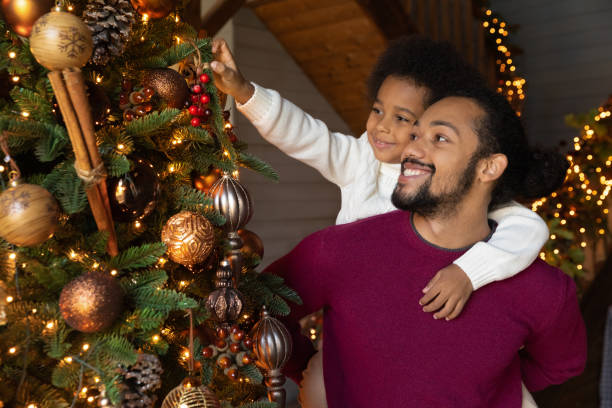 istock Smiling African American father piggy backing son, decorating Christmas tree 1284578736