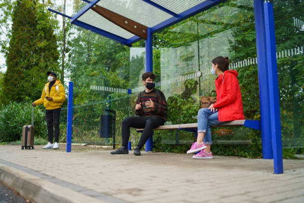 istock Young people talking on bus stop outdoors in town. Coronavirus concept. 1284582001