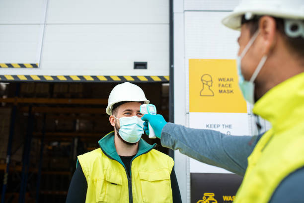 istock Workers with face mask in front of warehouse, coronavirus and temperature measuring concept. 1284583012