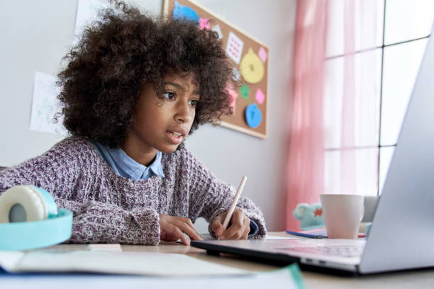 cute smart african american school pupil kid girl virtual distance learning online watching remote digital class lesson looking at laptop computer tech studying at home writing notes sitting at desk. - pre adolescent child student isolated little girls zdjęcia i obrazy z banku zdjęć