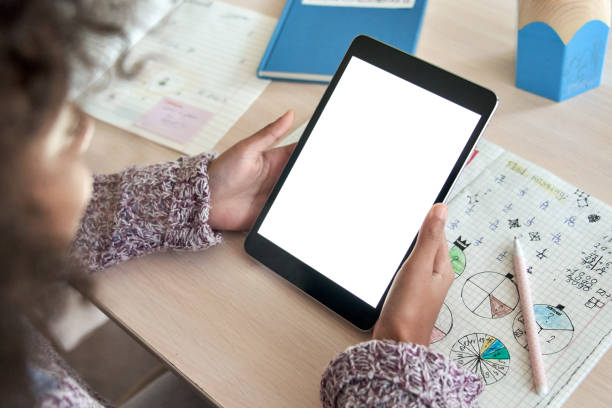 istock African american elementary school girl student distance learning online at home, elearning, watching web class holding digital tablet. Virtual education. Over shoulder close mock up screen view. 1284585943