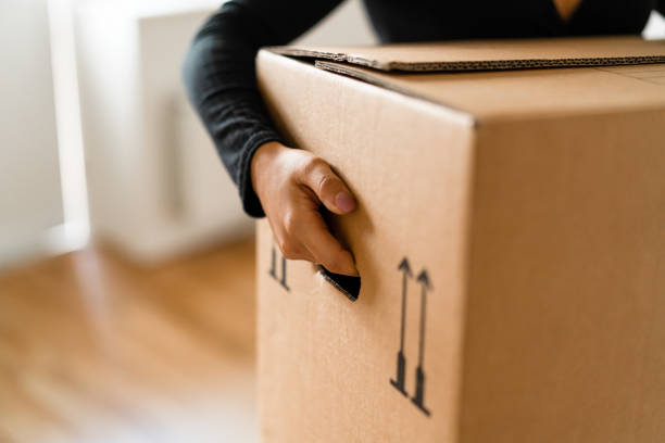 Woman carrying boxes into her new home A woman is carrying cardboard moving boxes into her new apartment. relocation stock pictures, royalty-free photos & images