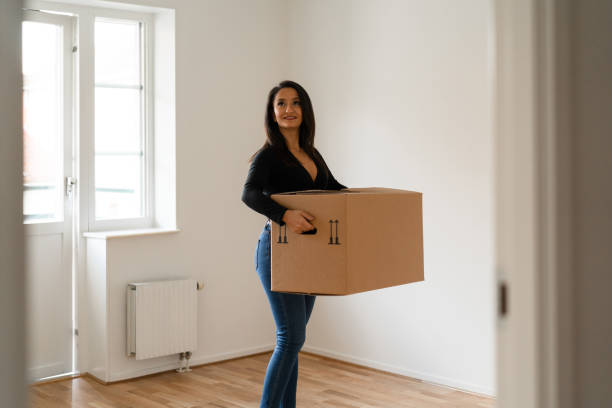 Woman carrying boxes into her new home A woman is carrying cardboard moving boxes into her new apartment. looking around stock pictures, royalty-free photos & images