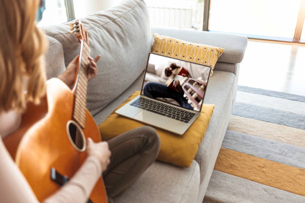 istock Woman practicing guitar with online video class using a laptop at home 1284589538