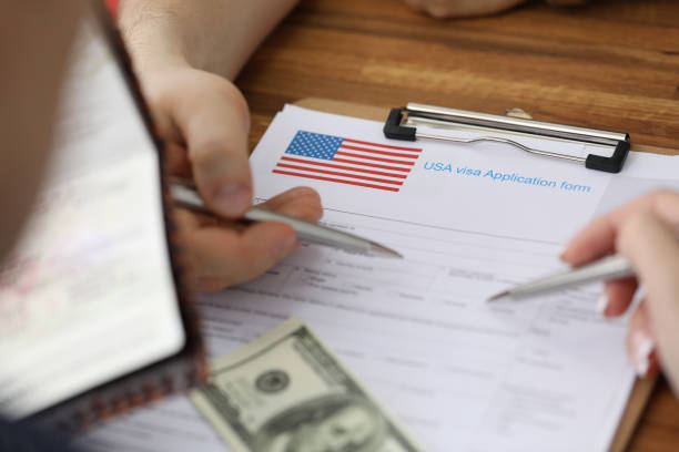istock Man with passport and dollars points with pen at documents in folder of embassy closeup 1284590535