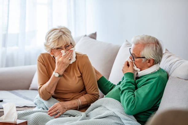 istock Mature couple sitting on sofa and blowing their noses 1284590543