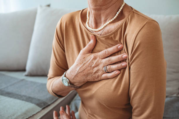 senior frau leidet unter brustschmerzen beim sitzen auf dem sofa zu hause. - overworked worried distraught front view stock-fotos und bilder