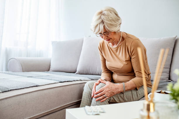 Senior woman holding the knee with pain. Old age, health problem and people concept - senior woman suffering from pain in leg at home. Elderly woman suffering from pain in knee at home. rheumatoid arthritis stock pictures, royalty-free photos & images