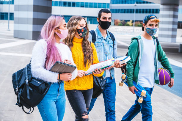 heureux amis interraciaux collège marchant dans le campus avec le masque de visage dans le temps covide-19 - concept au sujet du millénaire appréciant passer du temps ensemble à l’extérieur - face time photos et images de collection