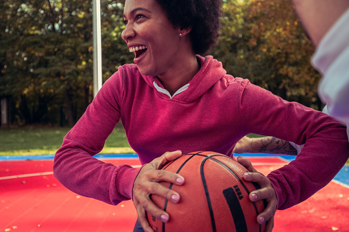 Friends are play basketball recreationally on weekends. The woman is bouncing the ball while the man is trying to stop her from getting to the hoop.