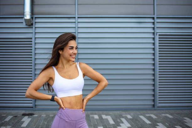 modelo fitness feminina em top branco e leggings roxas está posando ao ar livre. - underwear model - fotografias e filmes do acervo