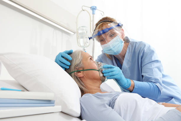 nurse puts oxygen mask on elderly woman patient lying in the hospital room bed, wearing protective gloves and visor medical mask, coronavirus covid 19 protection concept - respiratory system imagens e fotografias de stock