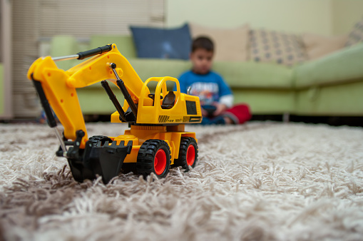 Kid playing with excavator toy on carpet at home blurred background