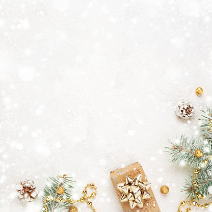 Christmas gift, green fir twigs, gold decoration on snowy white background. Copy space. New Year flat lay.