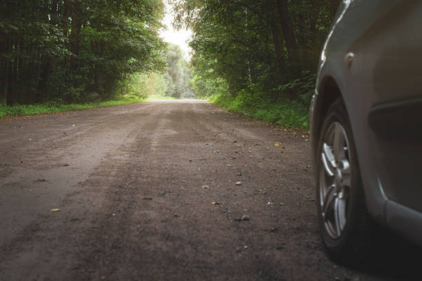 istock The old asphalt road through the forest after the rain. Sun's rays make their way through the leaves of the trees. Car on the side of the road. 1284597374