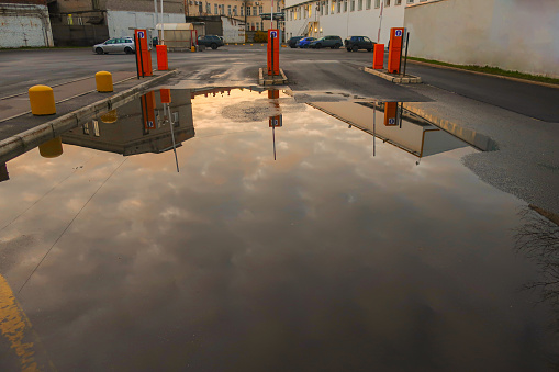 a large puddle on the asphalt after the rain with the reflected evening sky and clouds