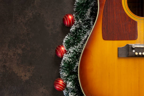 akustische gitarre und weihnachtsgirlanden-dekor mit roten kugeln auf dunkelbraunem hintergrund - dekorative stock-fotos und bilder