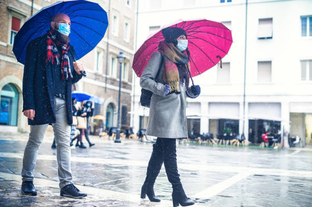 menschen mit gesichtsmaske zu fuß auf der straße stadt unter einem regenschirm im regen in der covid-19 zeit- neues normales lifestyle-konzept - kaltfilter - tail coat fotos stock-fotos und bilder