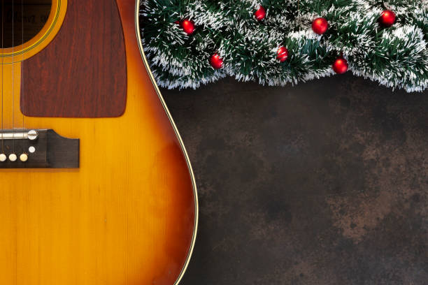 akustische gitarre und weihnachtsgirlanden-dekor mit roten kugeln auf dunkelbraunem hintergrund - dekorative stock-fotos und bilder