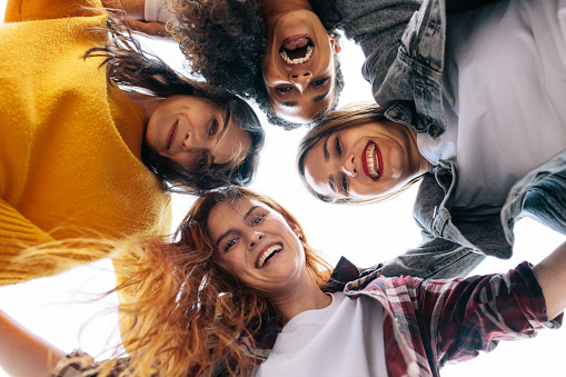 Low angle view of female friends forming a huddle and having fun. Group of women standing in a huddle looking at camera and smiling.